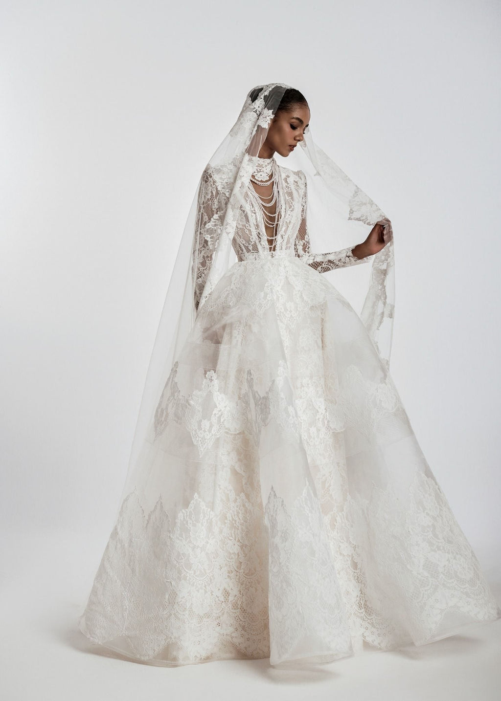Woman wearing a white lace wedding dress with a long veil on a white background