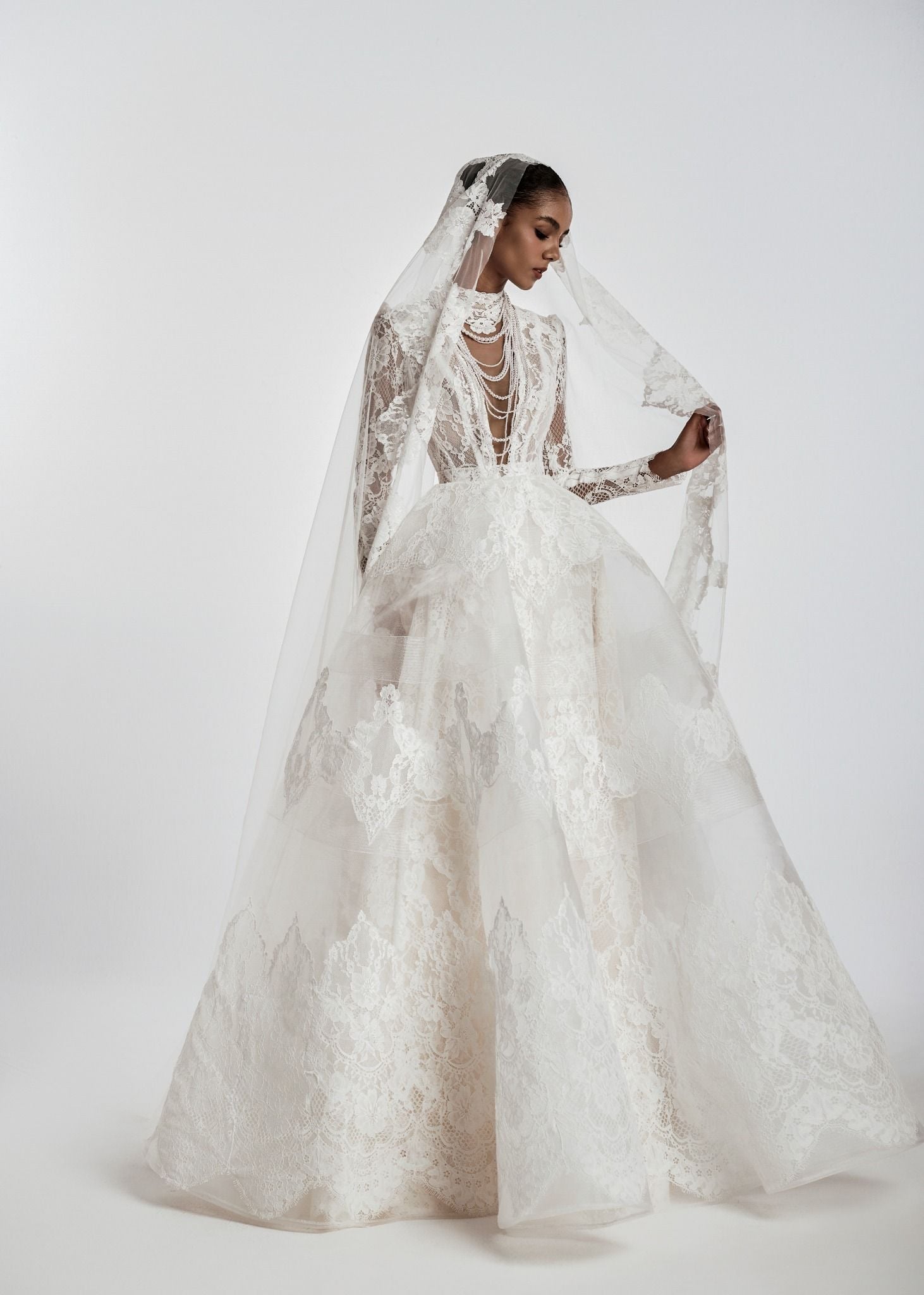 Woman wearing a white lace wedding dress with a long veil on a white background