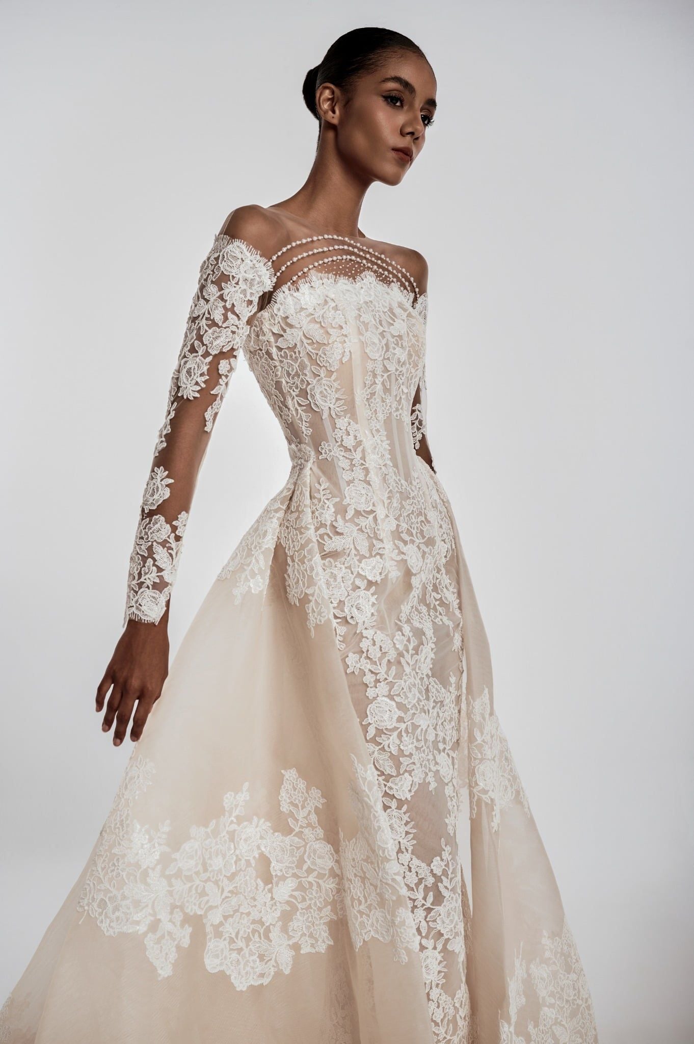 Model wearing a beige lace wedding dress with long sleeves on a white background