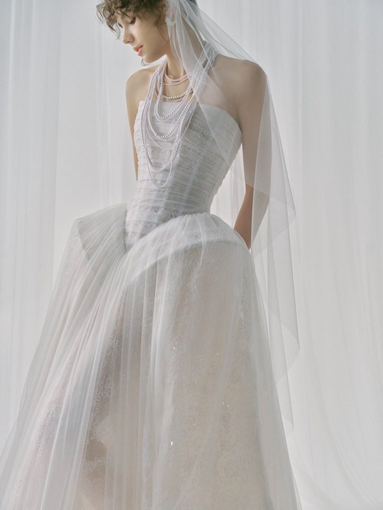 Woman wearing a light gray wedding dress with a veil against a white background