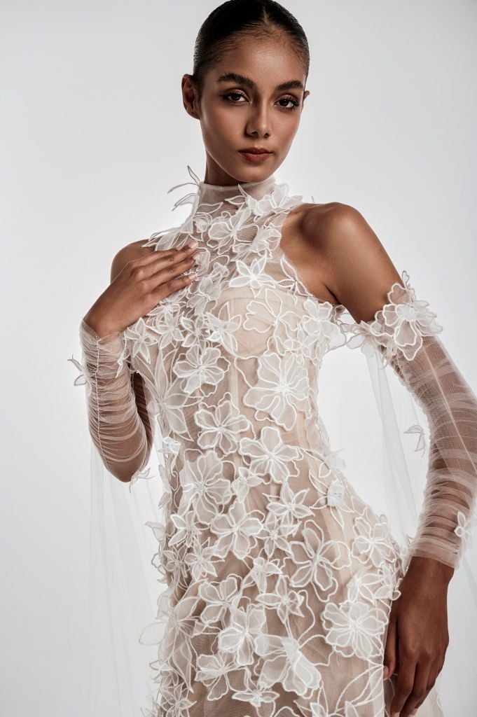 Model wearing a sheer white lace dress with long sleeves on a plain background